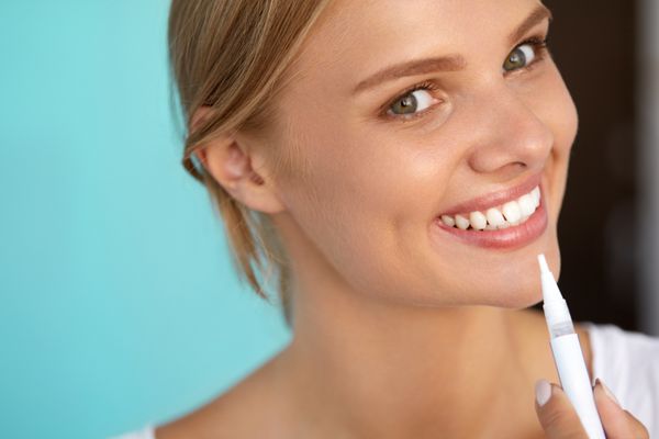 زنی با لبخند زیبا دندان های سالم با استفاده از قلم سفید کننده تصویر با وضوح بالا