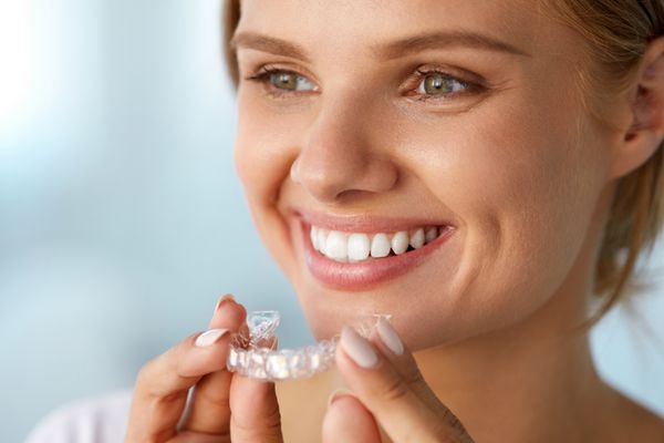 زن خندان با دندان های سفید که سینی سفید کننده دندان را در دست گرفته است تصویر با وضوح بالا
