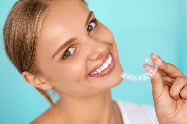 زن خندان با دندان های سفید که سینی سفید کننده دندان را در دست گرفته است تصویر با وضوح بالا