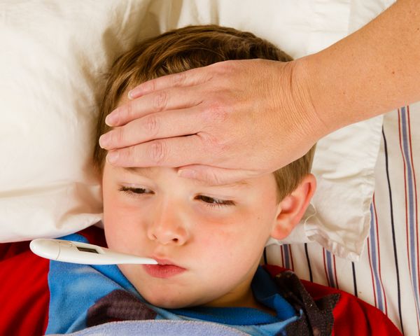 کودک پسر بیمار هنگام استراحت در رختخواب از نظر تب و بیماری معاینه می شود