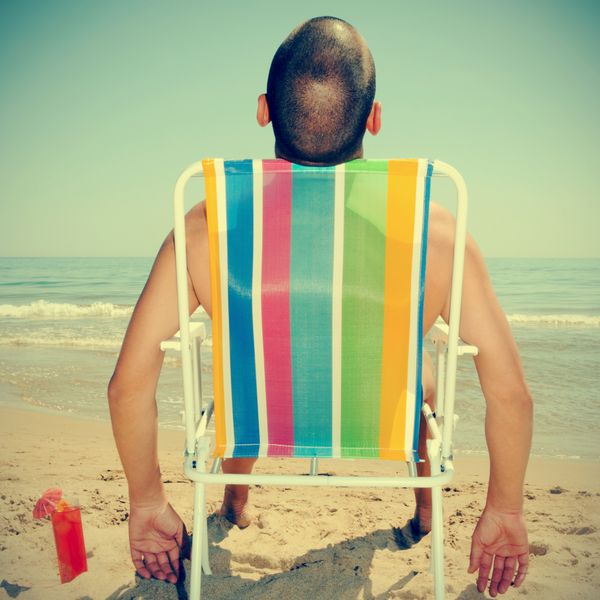 عکس مردی در حال آفتاب گرفتن روی صندلی روی صندلی در ساحل با دم با جلوه رترو