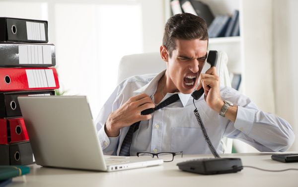 تاجر جوان عصبانی که در دفتر نشسته و روی تلفن جیغ می‌زند