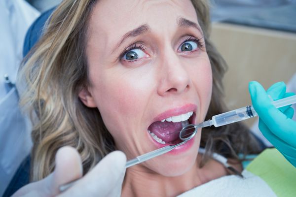 نمای نزدیک از زنی که دندان هایش را توسط دندانپزشک و دستیار معاینه می کند