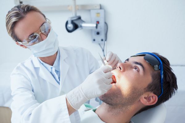 دندانپزشک زن در حال معاینه دندان های مرد در صندلی دندانپزشکی