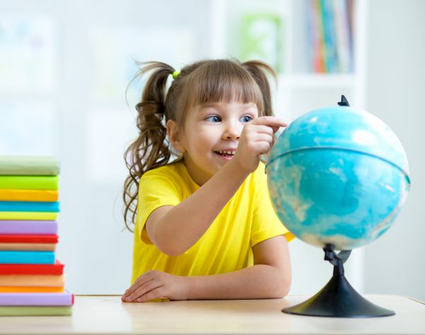 دختر بچه با اشاره به کره زمین و نشستن پشت میز با کتاب