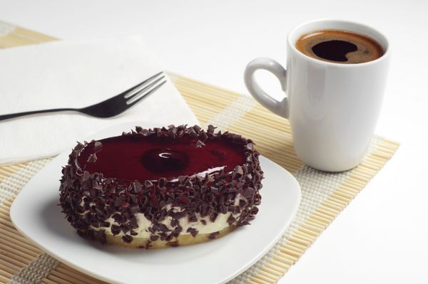کیک شکلاتی با ژله گیلاس و فنجان قهوه روی دستمال بامبو