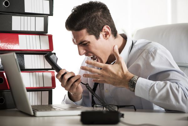 تاجر جوان عصبانی که در دفتر نشسته و روی تلفن جیغ می‌زند