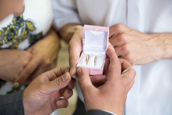 عروس و داماد در یک عروسی جعبه صورتی با حلقه های ازدواج طلایی را در دست گرفته اند