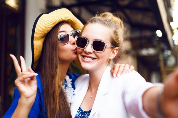 دختران زیبا و ناز در خیابان سلفی خنده دار می گیرند گونه ها را می بوسند با هم خوش می گذرانند شادی مثبت عشق دوستی خواهران