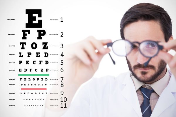 دکتری که کت آزمایشگاهی پوشیده است و در مقابل آزمایش چشم از عینک نگاه می کند