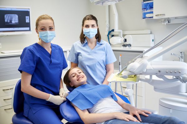 مفهوم مردم پزشکی دهان شناسی و مراقبت های بهداشتی - دندانپزشک زن شاد با دستیار و دختر بیمار در مطب کلینیک دندانپزشکی