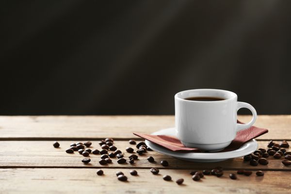 فنجان قهوه و دانه های قهوه روی میز چوبی در پس زمینه خاکستری