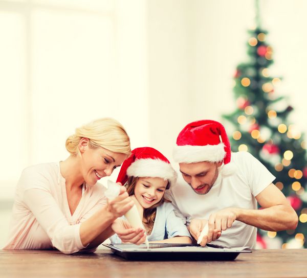 غذا خانواده کریسمس شادی و مفهوم مردم - خانواده خندان در کلاه کمکی بابا نوئل تزئین کوکی ها با لعاب
