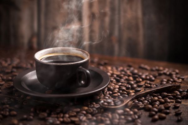 فنجان قهوه و دانه های قهوه روی پس زمینه چوبی