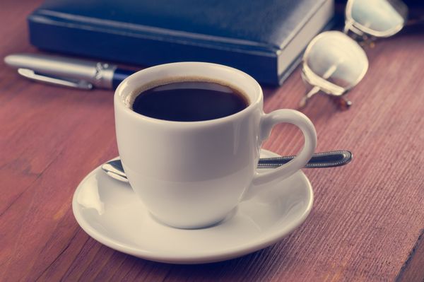رومیزی چوبی با فنجان قهوه صبحگاهی دفتر خاطرات خودکار و عینک فیلتر قدیمی بدون افراد متمرکز بر قهوه