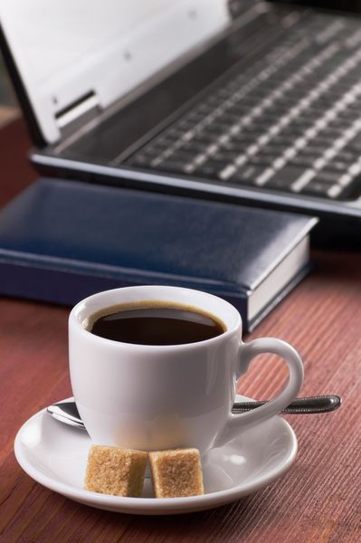 رومیزی چوبی با فنجان قهوه صبحگاهی لپ تاپ باز شده و دفترچه خاطرات با جلد خالی بدون افراد متمرکز بر قهوه