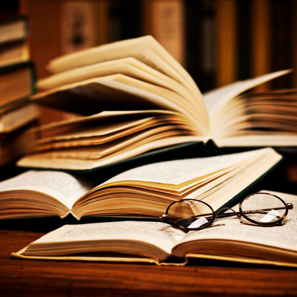 کتاب باز شده روی قفسه کتاب با یک عینک دراز کشیده است