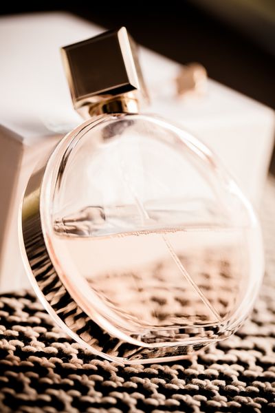 یک بطری گرد از عطر زنانه که در یک زاویه در برابر جعبه سفید و فرش بافت قرار گرفته است