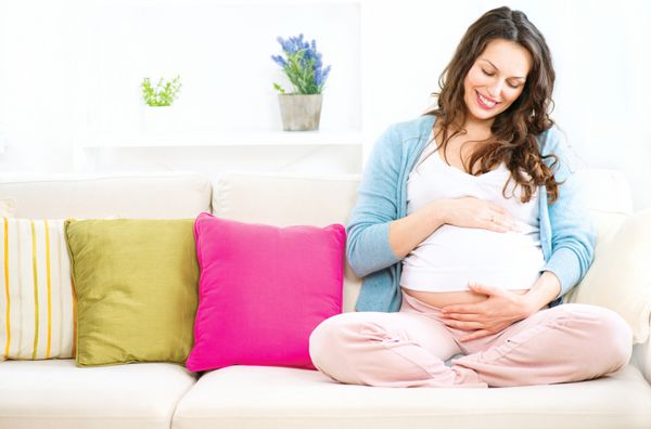زن باردار خندان شاد روی مبل نشسته و شکمش را نوازش می کند مامان منتظر بچه شکم زن باردار بارداری زن باردار زیبا مفهوم زایمان دوش بچه