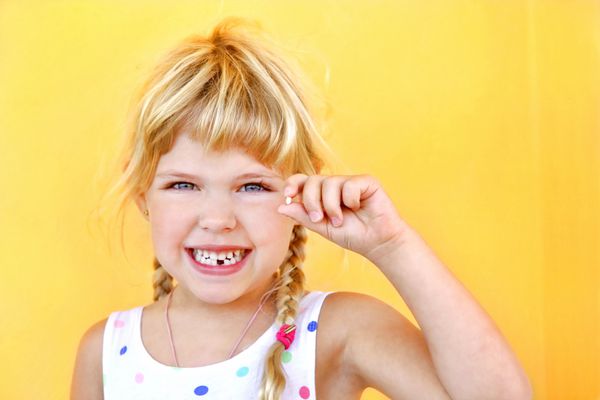 دختر خندان که دندان گم شده را در دست دارد