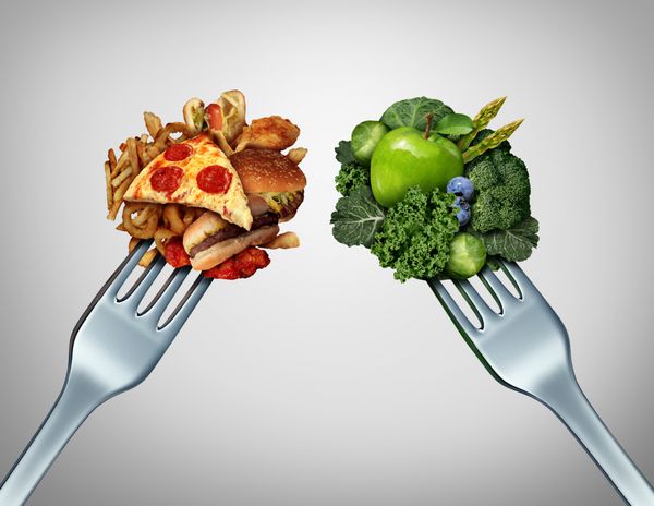 چالش رژیم غذایی و مفهوم تصمیم و انتخاب های تغذیه دوراهی بین میوه و سبزیجات سالم سالم و تازه یا فست فود غنی از کلسترول با دو چنگال شام که برای تصمیم گیری در مورد اینکه چه بخوریم با هم رقابت می کنند