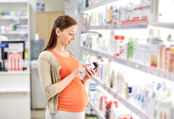 بارداری دارو داروسازی مراقبت های بهداشتی و مفهوم مردم - زن باردار خوشحال در حال خواندن برچسب روی شیشه دارو در داروخانه