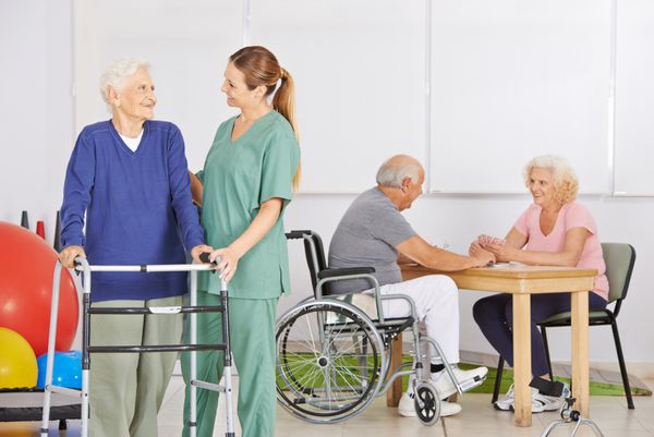 پرستار سالمند خندان با گروهی از افراد مسن در خانه سالمندان