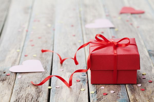جعبه هدیه با روبان پاپیونی قرمز و قلب کاغذی روی میز چوبی برای روز