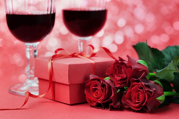 جعبه هدیه گل رز قرمز و دو لیوان در پس زمینه تعطیلات برای روز