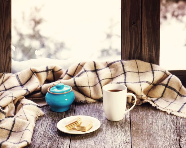 فنجان قهوه یا چای سفید گلدان آبی و چهارخانه پشمی که روی طاقچه پنجره چوبی سبک قرار گرفته است مفهوم زمستانی آسایش و آرامش عکس با جلوه فیلتر یکپارچهسازی با سیستمعامل
