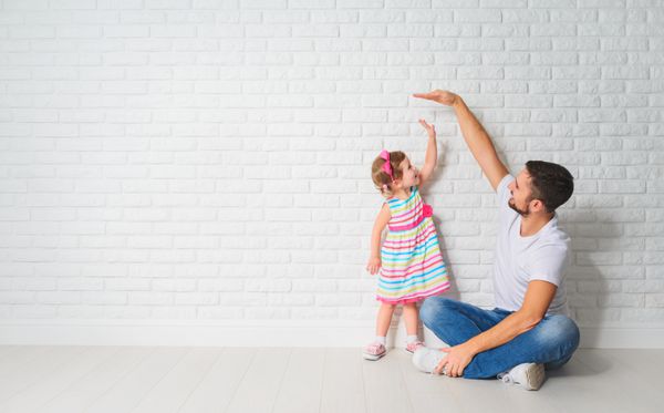 مفهوم پدر رشد دختر فرزندش را روی یک دیوار آجری خالی اندازه می گیرد