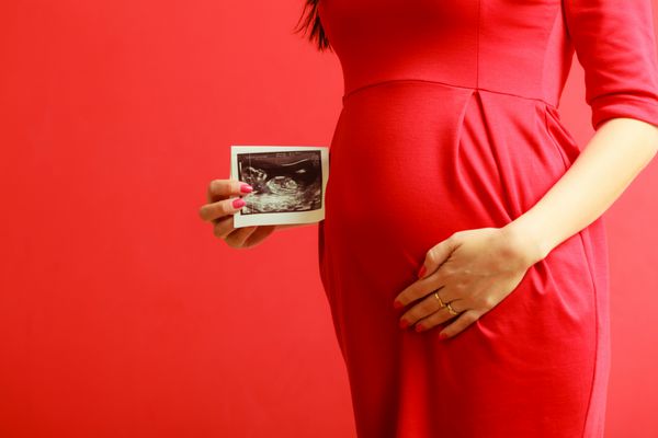 مفهوم جدید زندگی بارداری مادر شدن و خوشبختی شکم نزدیک زن باردار با لباس قرمز ظریف اسکن سونوگرافی در دست در داخل خانه