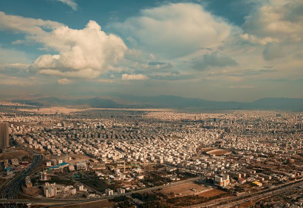 نمای هوایی شهر تهران در مقابل آسمان آبی با ابرهای سفید کرکی بالای برج میلاد