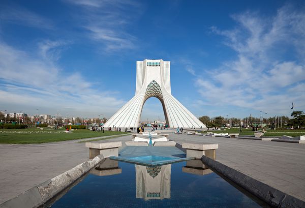 بنای یادبود آزادی و انعکاس آن در مسیرهای آبی میدان آزادی تهران در برابر آسمان آبی و ابرهای سفید