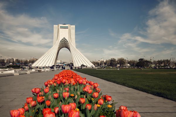 بنای یادبود آزادی پشت ردیفی از لاله های قرمز در تهران در فصل بهار ویرایش شده با فیلتر قهوه ای وینتیج
