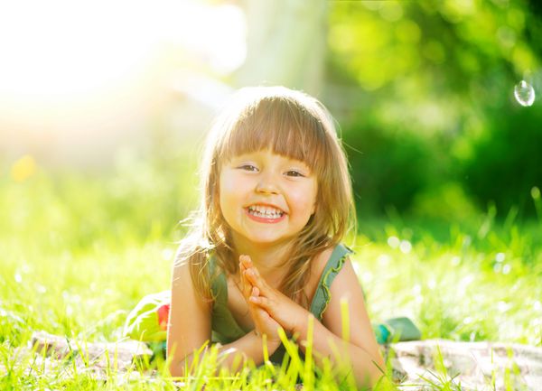 پرتره یک دختر کوچک خندان که روی چمن سبز دراز کشیده است کودک سه ساله ناز در حال لذت بردن از طبیعت در فضای باز بچه سالم و بی خیال بیرون در پارک تابستانی