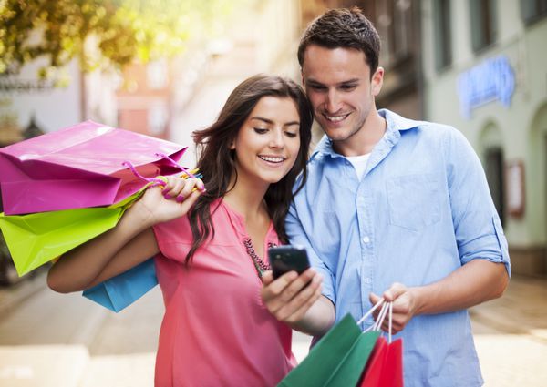 زوج جوان با کیف خرید با استفاده از تلفن همراه