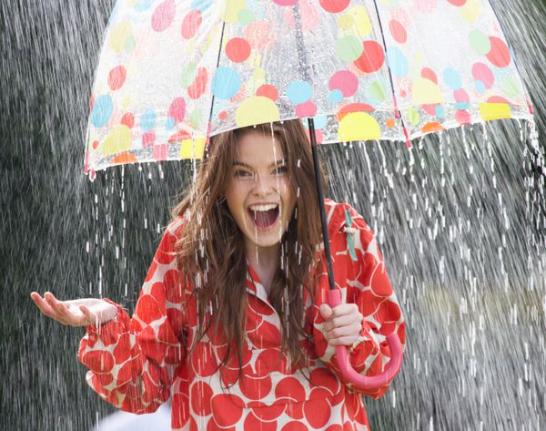 دختر نوجوانی که از باران زیر چتر پناه گرفته است