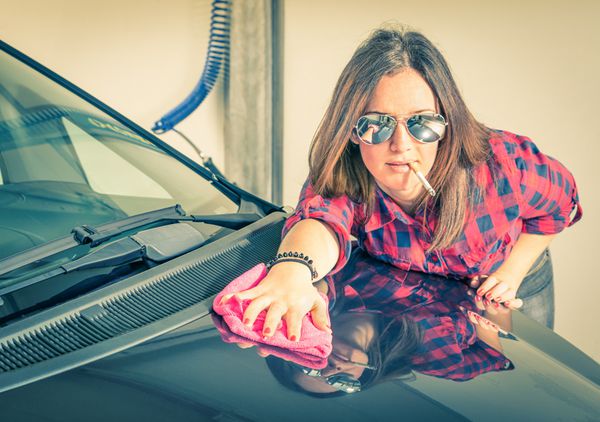 زن جوان زیبا در حال تمیز کردن ماشینش در کارواش