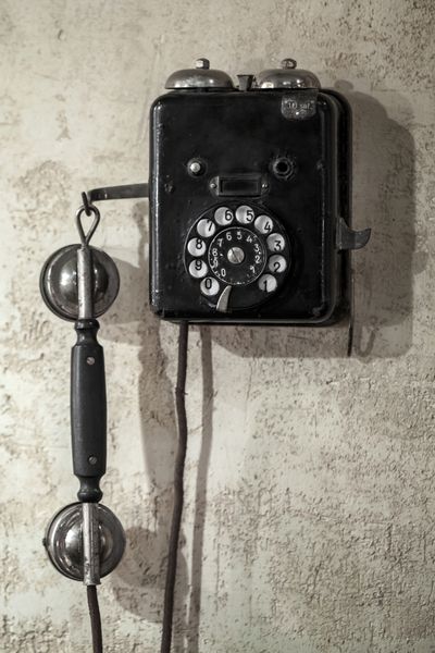 تلفن مشکی قدیمی که روی دیوار بتونی خاکستری قدیمی آویزان شده است