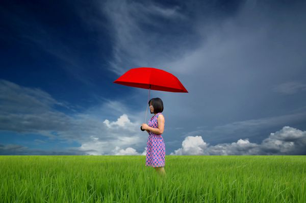 زن جوان با چتر قرمز در زمین سبز زیر باران