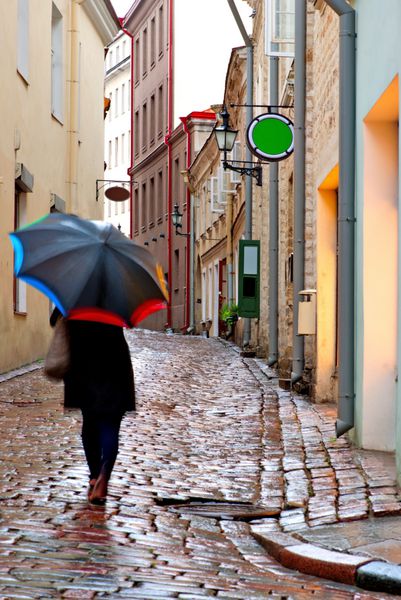 زنی با چتر در خیابان باریک با سنگفرش های خیس در تالین استونی
