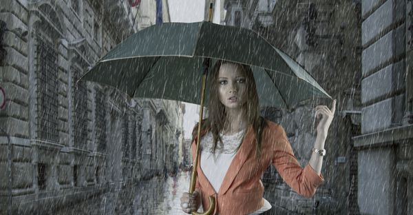 زن جوان زیبا با چتر سبز در حال تعمیر از باران در یک شهر قدیمی