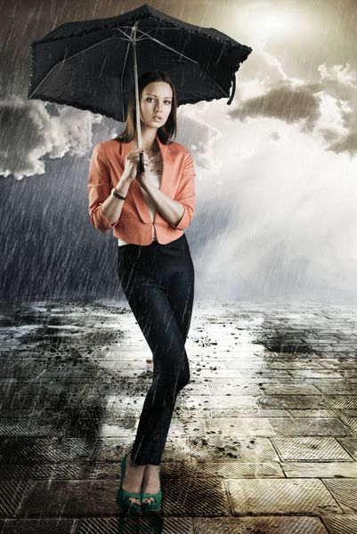 زن جوان زیبا با چتر تیره جلوی دوربین است به لنز نگاه می کند و با دو دست چتر را می گیرد