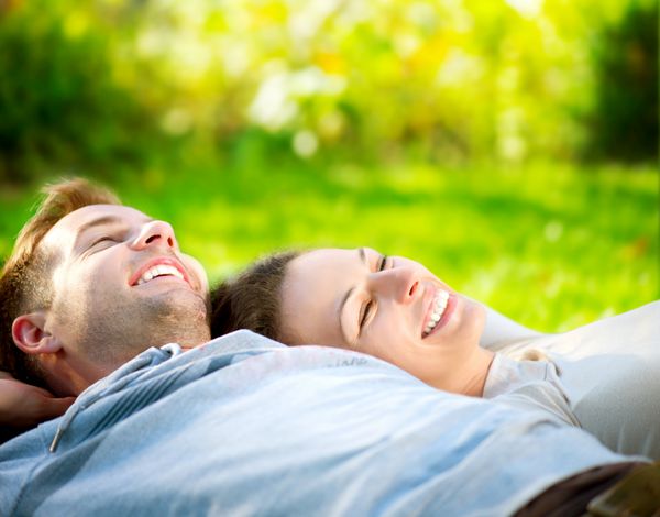 زوج خندان شاد در حال استراحت روی چمن سبز پارک زوج جوان دراز کشیده روی چمن در فضای باز