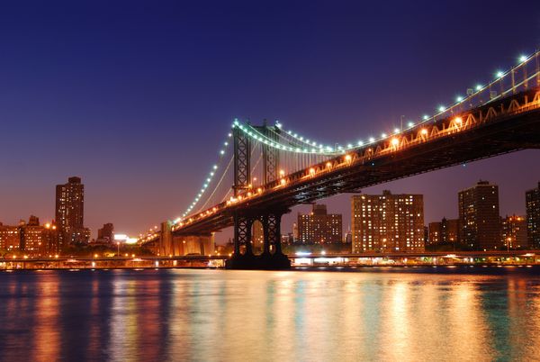 پل منهتن شهر نیویورک بر روی رودخانه هادسون با نمای شب بعد از غروب آفتاب که با نورهایی که از بروکلین مشاهده می‌شود افق دارد