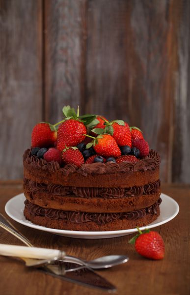کیک شکلاتی با آیسینگ و توت تازه در زمینه چوبی