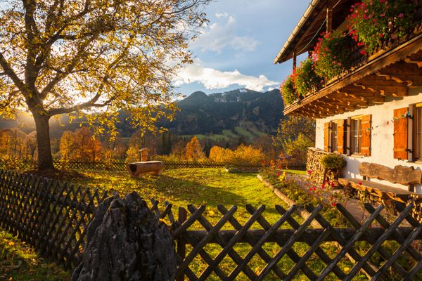 یک خانه معمولی باواریایی با باغچه در پس زمینه غروب خورشید و منظره کوهستانی