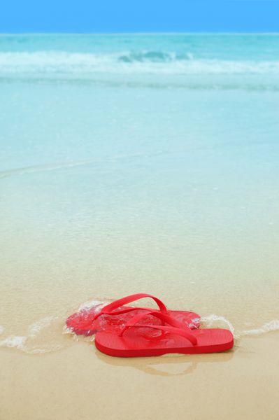 دمپایی قرمز روی ماسه ساحل مفهوم تعطیلات تابستانی