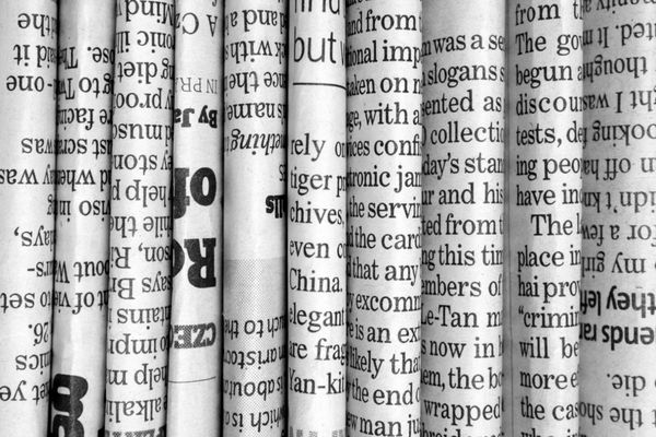 یک پس‌زمینه سیاه و سفید از روزنامه‌های انگلیسی زبان که در حالت عمودی روی هم چیده شده و تا شده و در نمای نزدیک مشاهده می‌شود
